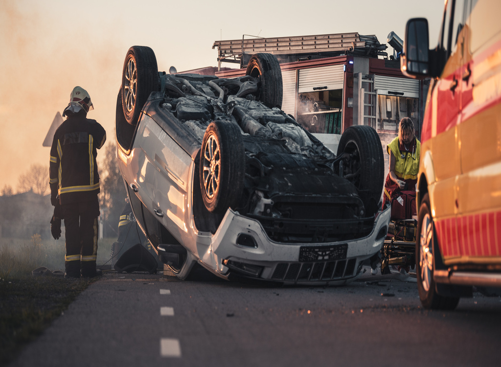Horrific Traffic Accident Rollover Smoking and Burning Vehicle Lying on its Roof in the Middle of the Road after Collision. Daytime Crash Scene with Damaged Car.